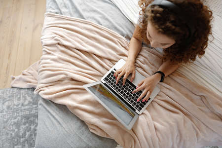 Portrait of a young curly woman using laptop in bed at homeの写真素材