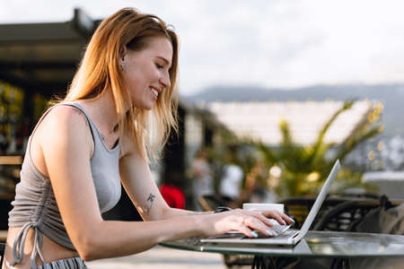 Happy beautiful young woman working on laptop in street cafe