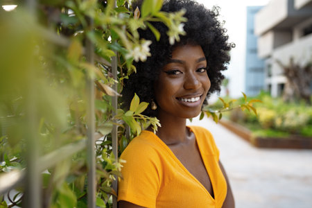 Portrait of a beautiful young african american woman posing against backdrop of green hedgeの写真素材