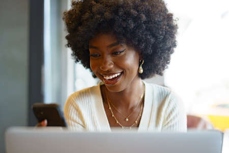 Smiling young african woman sitting with laptop in cafeの写真素材