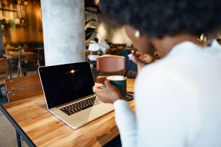 Smiling young african woman sitting with laptop in cafeの写真素材