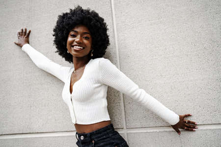 Black woman with afro hair posing in front of a gray concrete wallの写真素材