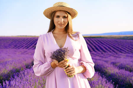 Young woman in dress holding bouquet of flowers standing in lavender fieldの写真素材