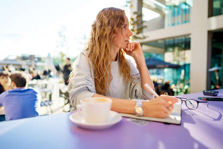 Casual woman sitting at table and taking notes in notebook .on the cafe terraceの写真素材