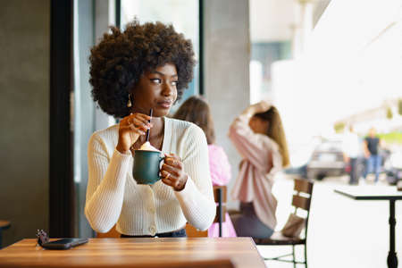 Young afro woman taking break and drinking coffee in cafeの写真素材