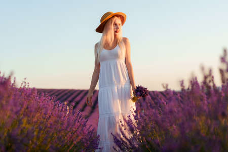 Young woman in long white dress standing in lavender fieldの写真素材