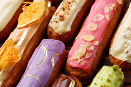 Assortment of sweet and colorful eclairs on wooden background
