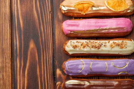Assortment of sweet and colorful eclairs on wooden background