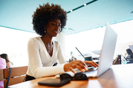 Smiling young african woman sitting with laptop in cafe