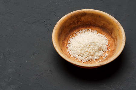Heap of dry rice in a bowl on black background, lack of food, hunger conceptの写真素材