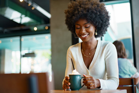 Young afro woman taking break and drinking coffee in cafeの写真素材