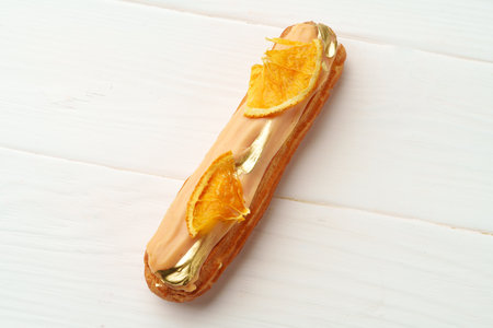 Eclair with orange icing on white wooden background