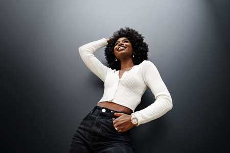 Fashionable young beautiful woman with afro hairstyle posing on the black wallの写真素材