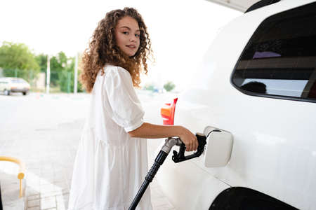 Young curly woman refueling car at gas stationの写真素材