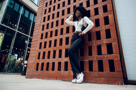 Portrait of young curly charming black female standing against brick wallの写真素材