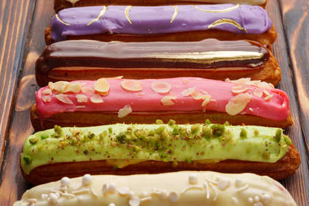 Assortment of sweet and colorful eclairs on wooden backgroundの写真素材