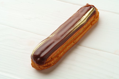 Chocolate eclair on white wooden background, close up