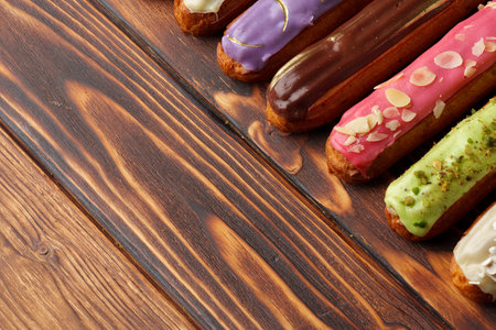 Assortment of sweet and colorful eclairs on wooden background