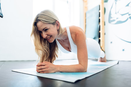 Middle-aged woman stretching on exercise mat at a gym.
