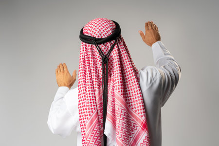 Back view of young Arab man standing on gray background
