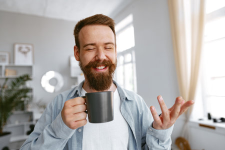 Young bearded man smiling and drinking coffee at homeの写真素材