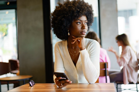 Young afro woman using mobile phone at coffee shopの写真素材