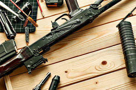 Black disassembled shotgun and cleaning tools on wooden table .