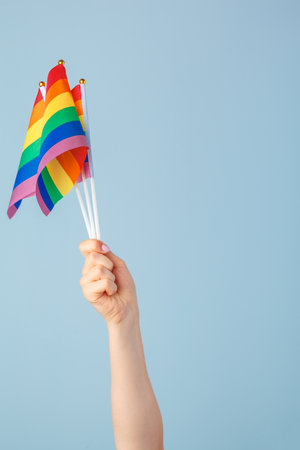 Closeup of a hand waving a small rainbow flag against a light blue backgroundの写真素材
