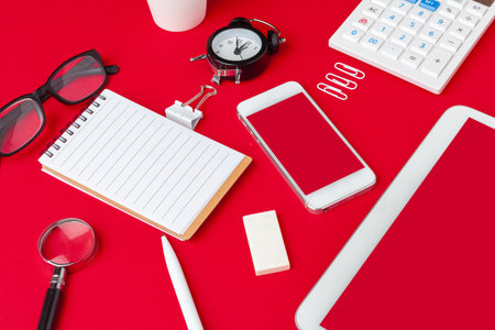 Red office desk table with blank notebook, keyboard and supplies. Top view with copy space. Flat...
