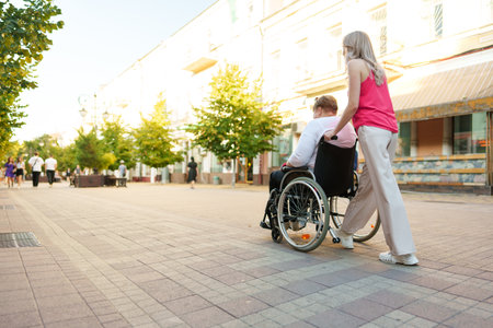 Young female caregiver pushing wheelchair with female person with disability across city streetの写真素材