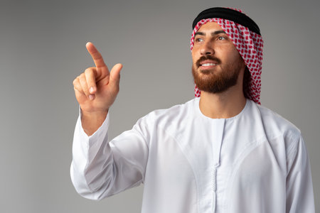 Young Arab man pointing hand to copy space on gray backgroundの写真素材
