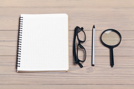 Magnifying glass and notebook on wooden tableの写真素材