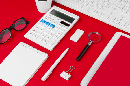 Red office desk table with blank notebook, keyboard and supplies. Top view with copy space. Flat...