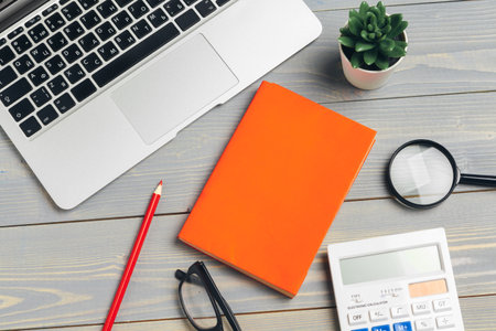 Angled View of laptop Computer Keyboard and glasses with Various Office Supplies on wooden Deskの写真素材