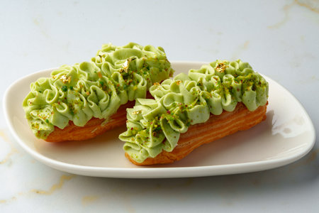 Eclair cake with pistachio glaze on white plate