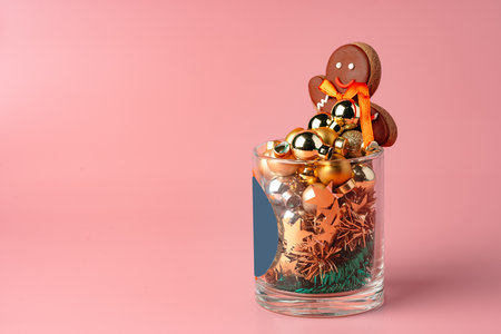 Glass with Christmas decorations on pink pastel background