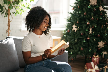 African woman reading book at home sitting on sofa