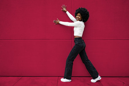Smiling fashionable american woman walking on city street. Color of the year 2023, viva magenta.