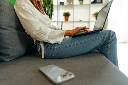 Woman using laptop computer while sitting on a sofa at home.の写真素材