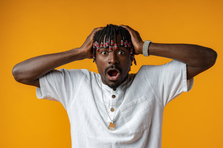 Shocked african man opening mouth widely on yellow studio background