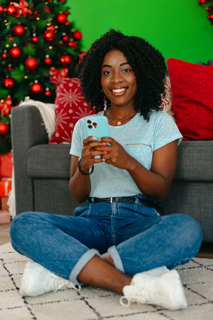 Happy black woman using smartphone in a room decorated for Christmasの写真素材