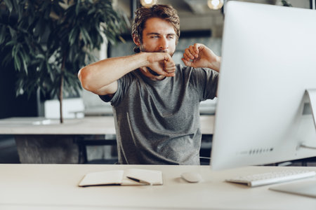 Tired businessman working on his computer in open space officeの写真素材