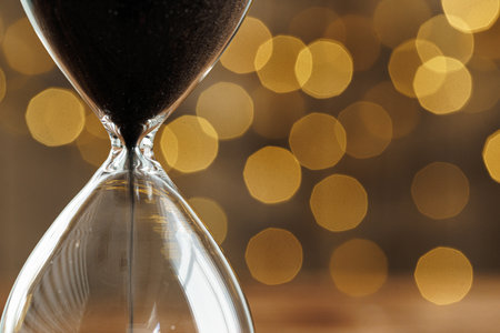Hourglass on wooden desk against blurred lights
