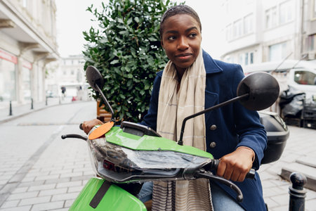Portrait of a young and stylish african woman with a moped in the city