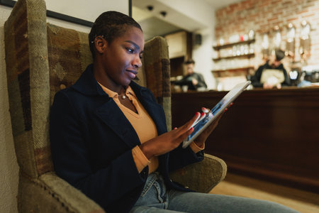 Young african woman sitting in arm-chair and using digital tablet