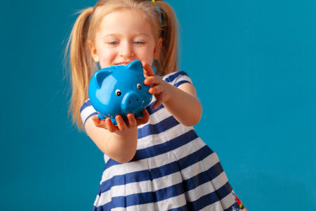 Little girl with piggy bank moneybox against blue backgroundの写真素材