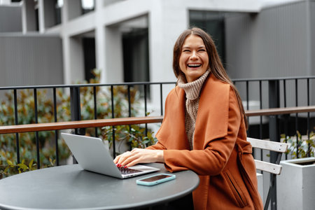 Young woman working with her laptop sitting at the table in the streetの写真素材