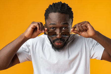 Close up of young african man in sunglasses standing against yellow background