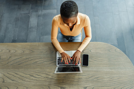 Young african woman freelancer working on laptop while sitting in coworkingの写真素材