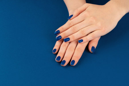 Female hands with manicure of classic blue color on blue backgroundの写真素材